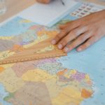 A hand uses a wooden ruler on a world map, planning international travel