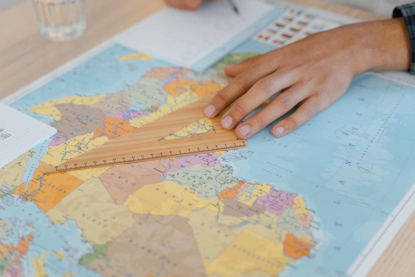 A hand uses a wooden ruler on a world map, planning international travel
