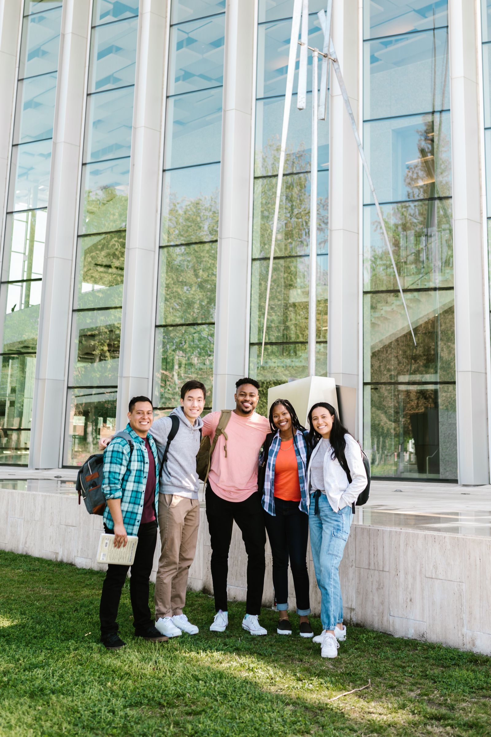 Cheerful group of diverse students standing outside a modern university building